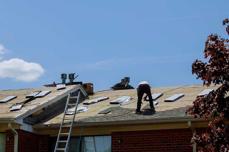 Homeowner examining roof gutters from the ground beside a snow-ready house