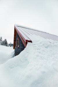 Snow-covered roof with a thick ice ridge along the eaves, visible gutters, and winter sunlight.