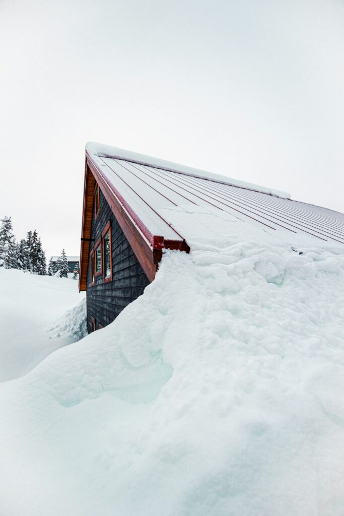 Snow-covered roof with a thick ice ridge along the eaves, visible gutters, and winter sunlight.